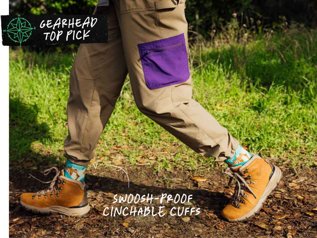 A person wearing cargo shorts, fun socks, and leather boots walks on a trail. Text overlay reads: Gearhead Top Pick, swoosh-proof cinchable cuffs.
